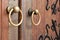 Closeup of two antique copper ornate door knockers over an aged wooden door.