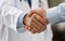 Closeup of two hands shaking, one in a white doctor\\\'s coat and the other wearing a blue shirt