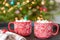 Closeup of two holiday mugs of hot chocolate by the Christmas tree