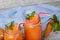 Closeup of two mason jars full of carrot smoothie with basil, sappy mint and carrot on a light blurred background.