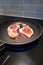 Closeup of Two Pork Chops Frying in a Non-Stick Frying Pan on an Induction Stove Top