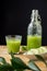 Closeup of unfocused leaves with bottle and glass with cucumber and mint juice on black background, vertical