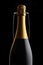 Closeup of an unopened bottle of Champagne in front of a flute against a black background