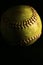 Closeup of a used, yellow softball on a black backround.