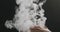 Closeup vapor rises through man hand from bottom on black background