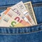 Closeup of various countries banknotes peeking out of blue jeans back pocket