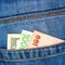 Closeup of various countries hundred banknotes peeking out of blue jeans back pocket