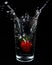 Closeup vertical shot of a strawberry being dropped into a glass of water and causing a splash.