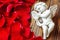 Closeup view of beautiful cupid with the trumpet, angel decorative figurine near red rose petals on wooden background.