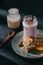 closeup view of berry smoothie with drinking straw, slices of energy bar, jam and walnuts on plate, spoon and bottle of yogurt