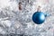 Closeup view of a blue matte ball hanging on a silver artificial Christmas tree for a family holiday. Selective focus