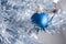 Closeup view of a blue matte ball hanging on a silver artificial Christmas tree. Selective focus. Blurred background