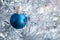 Closeup view of a blue matte ball hanging on a silver artificial Christmas tree. Selective focus. Blurred background