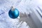 Closeup view of a blue matte ball hanging on a silver thread on a white artificial Christmas tree with copy space. Selective focus