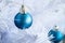 Closeup view of a blue matte ball hanging on a silver thread on a white artificial Christmas tree. Selective focus