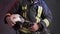 Closeup view of a brave firefighter in special uniform holds protective helmet standing against a gray wall