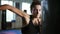 Closeup view of caucasian female boxer hitting the boxing bag with her hands in gloves in the gym alone. Tough power