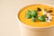 Closeup view of creamy pumpkin fall soup in craft paper food container against light background with copy space