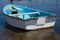 Closeup View of Dinghy Paddle Boat on Clear Water. Oar, rusty Chain and Rope Resting inside the Blue Watercraft. Vessel