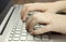 Closeup view of a hand with fingers typing on a keyboard Silver laptop lying on a wooden mat