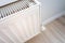 Closeup view of a home heating radiator in a living room with wooden floor and light wall