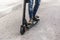 Closeup view of the legs of a boy climbed on a black electric scooter on a street