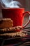 Closeup view of a piece of cookie next to a red cup of hot coffee on a colorful tablecloth