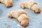 A closeup view of a sweet ruddy croissants with sugar lying on a parchment paper covered with flour. Baked bagels from a curd