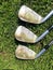 A closeup view of three golf irons with dirty grooves that need cleaning