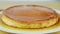 Closeup view at whole round soft flan with caramel syrup served on white plate