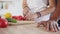 Closeup view of woman`s hands cutting tomato while his boyfriends hands on the table. Happy multiethnic couple in the