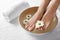 Closeup view of woman soaking her feet in dish with water and flowers on white towel. Spa treatment