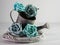 Closeup of a vintage silver watering pot decorated with blue roses against a grey blurry background