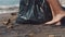 Closeup of volunteer picking up plastic bottle on the black sand beach into black plastic bag. Volunteer cleaning the