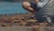 Closeup of volunteers sit and picking up garbage on the beach. Cleaner collecting garbage on the sea beach into black