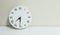 Closeup white clock for decorate show half past seven or 7:30 a.m. on white wood desk and cream wallpaper textured background with