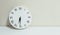 Closeup white clock for decorate show half past six or 6:30 a.m. on white wood desk and cream wallpaper textured background with c
