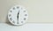 Closeup white clock for decorate show half past twelve or 12:30 p.m. on white wood desk and cream wallpaper textured background wi