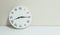 Closeup white clock for decorate show a quarter past eight or 8:15 a.m. on white wood desk and cream wallpaper textured background