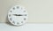 Closeup white clock for decorate show a quarter past nine or 9:15 a.m. on white wood desk and cream wallpaper textured background