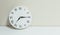Closeup white clock for decorate show a quarter past seven or 7:15 a. m. on white wood desk and cream wallpaper textured backgroun