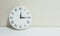 Closeup white clock for decorate show a quarter past twelve or 12:15 a.m. on white wood desk and cream wallpaper textured backgrou