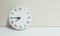 Closeup white clock for decorate show quarter to eight or 7:45 a.m. on white wood desk and cream wallpaper textured background wit