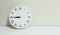 Closeup white clock for decorate show a quarter to nine or 8:45 a.m. on white wood desk and cream wallpaper textured background wi
