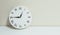 Closeup white clock for decorate show a quarter to one p.m. or 12:45 p.m. on white wood desk and cream wallpaper textured backgrou