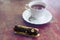 Closeup at white cup with black tea and eclair with chocolate
