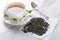 Closeup of white cup of green hot tea with jasmine flowers, vintage spoon, dry leaves of tea on the white table