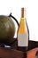 Closeup of a White Wine bottle with a blank label in a wood crate with antique world globe, over white