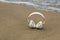 Closeup of white wireless headphones on the seashore with waves in the background