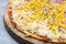 Closeup of a whole delicious pizza with melted cheese, corn and onions on a board